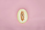 Honeydew melon half showcasing its smooth green flesh and seeds on a pink background.