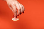 Hand holding a lemon slice against a vibrant orange background.