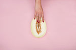Fresh cantaloupe melon cut in half, showcasing its orange flesh and seeds on a pink background.