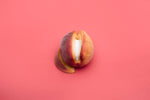 Fresh peach with a vibrant pink background, showcasing its juicy flesh and smooth skin.