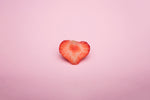 Heart-shaped strawberry slice on a pink background.