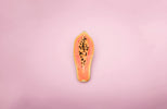 Papaya fruit with vibrant orange flesh and black seeds on a pink background.