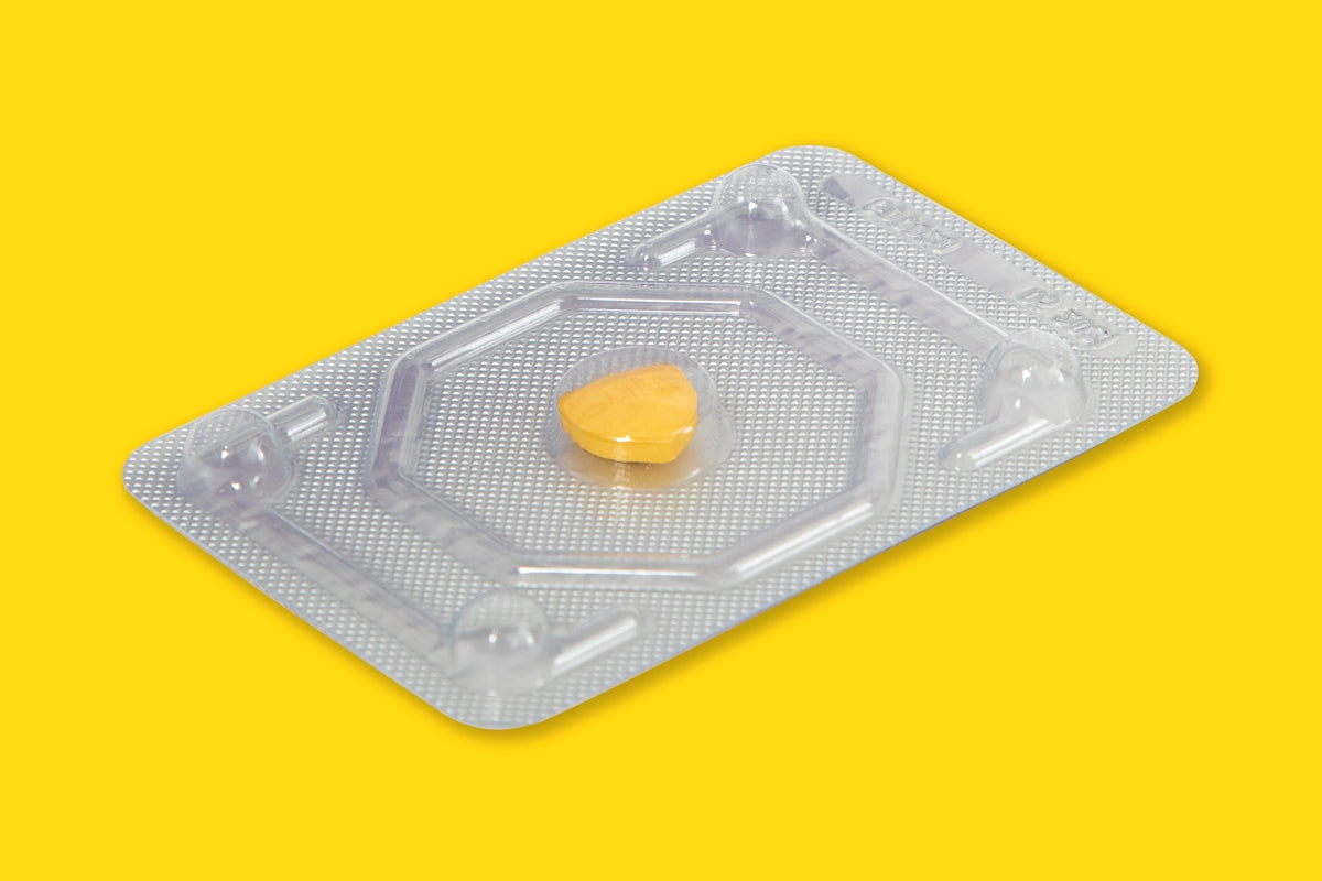 Yellow dietary supplement capsule on a clear blister pack against a bright yellow background.