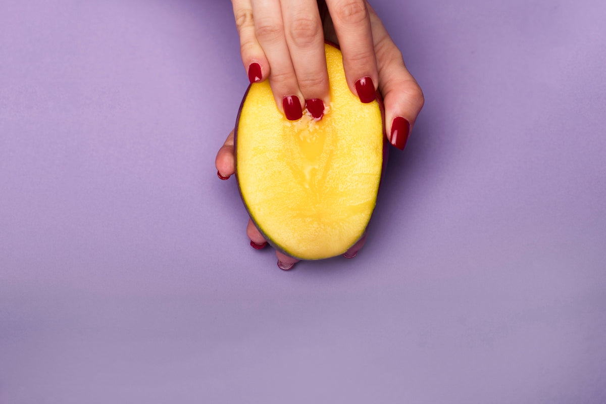 Mango slice held in hand with red nails against a purple background.