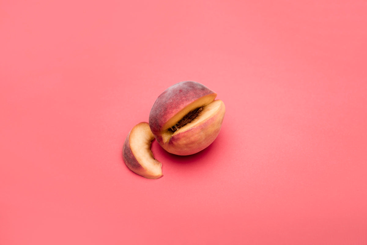 Fresh peach with a slice on a pink background.