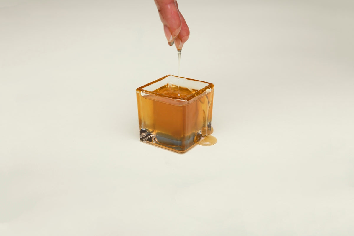 Honey jar with golden honey being drizzled from a finger.
