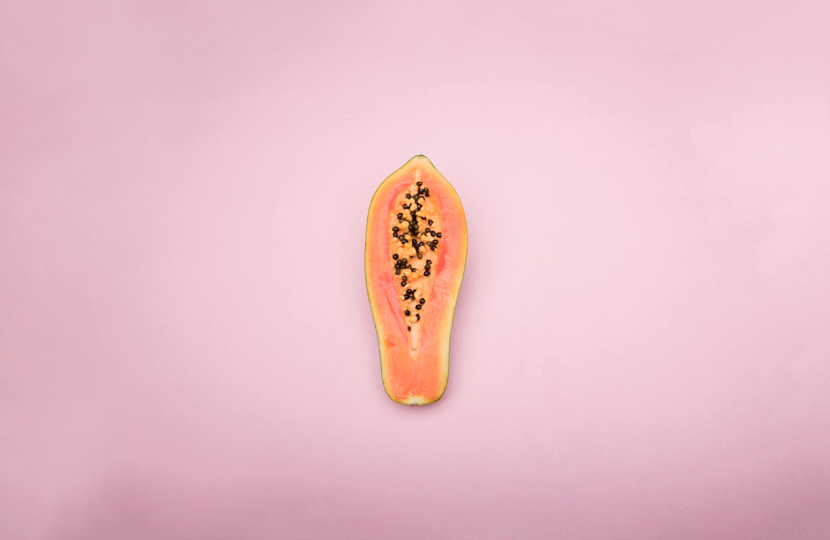 Papaya fruit with vibrant orange flesh and black seeds on a pink background.
