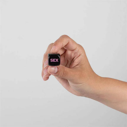 Hand holding a black die with the word 'SEX' from the 6 Die Play Sex Game (ES/EN/DE/FR/NL/PT/IT), a playful couples' dice game.