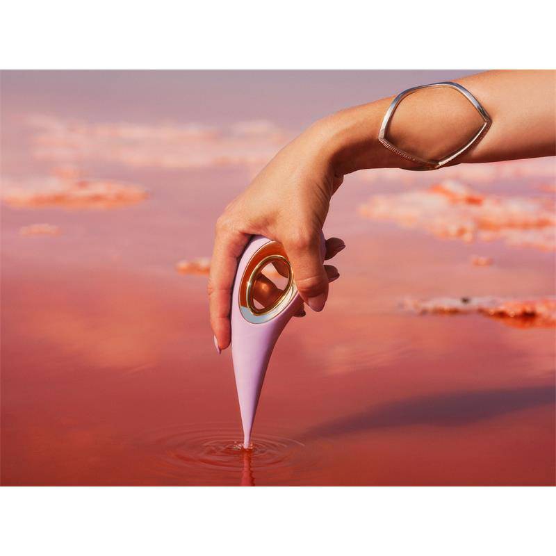 Pink sleek clitoris stimulator with ergonomic design held by hand over reflective pink surface.