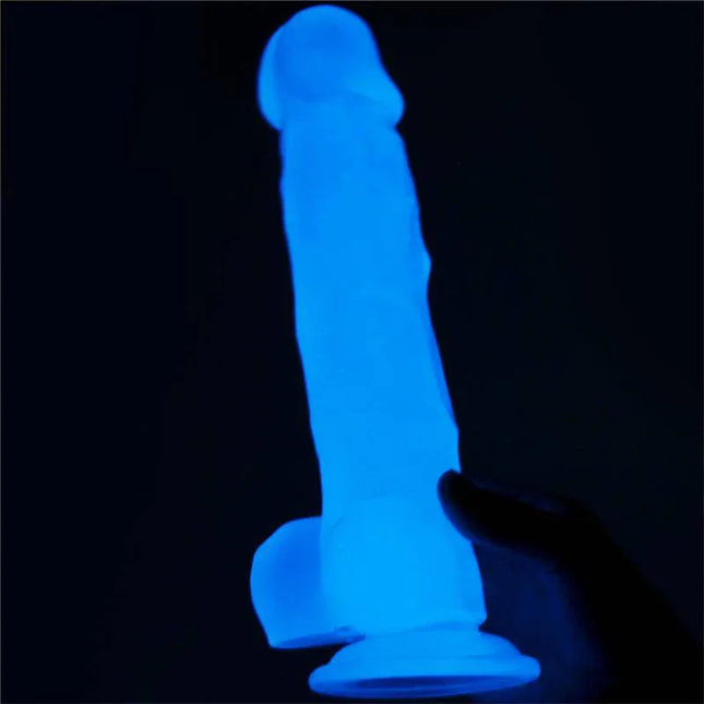 Dildo 8.5 Lumino Blue Light glowing in the dark held by a hand, showcasing its lifelike texture and vibrant blue color.