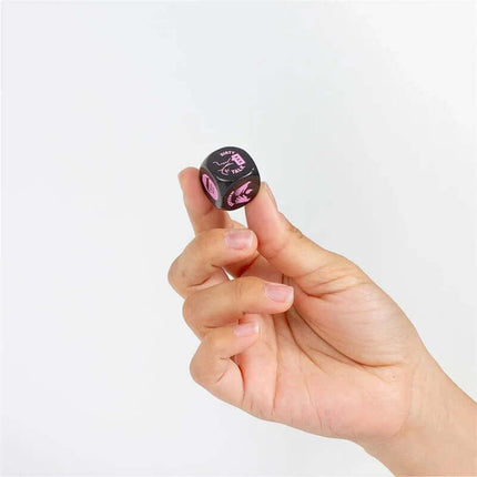 Hand holding a Foreplay Die 20 mm, black die with pink symbols, enhancing spontaneity and communication in intimate moments.