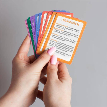 Hands holding colorful cards from Game Out of Routine (FR/PT) for couples' relationship improvement and fun activities.