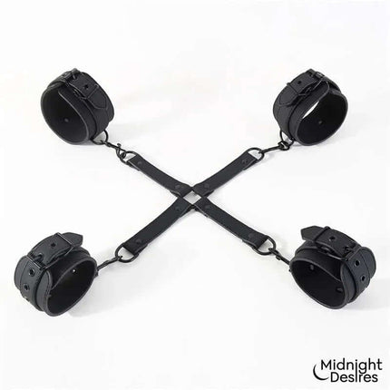 Hogtie Cross Bar Hand and Ankle Cuffs in black vegan leather from Midnight Desires, showing cross-shaped spreader for restrained play.