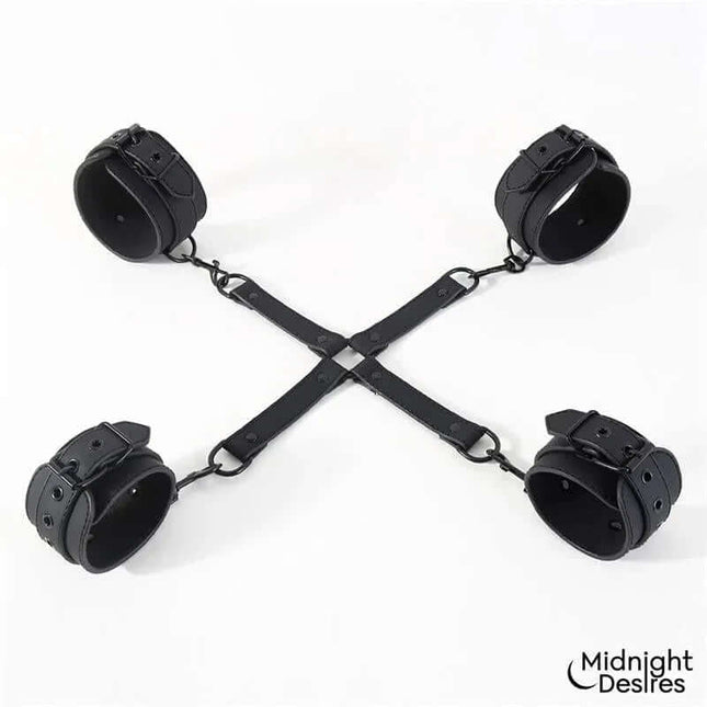 Hogtie Cross Bar Hand and Ankle Cuffs in black vegan leather from Midnight Desires, showing cross-shaped spreader for restrained play.