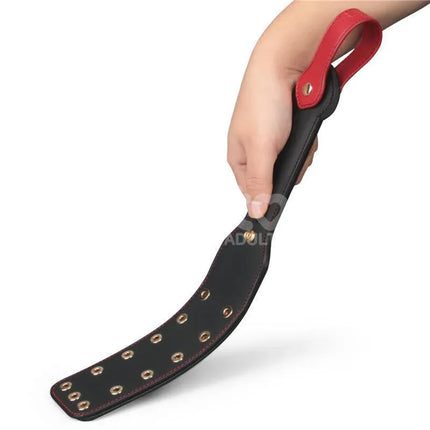 Hand holding Rebellion Reign Paddle Dual-Branch 15 with black PU material and red handle for intimate play.