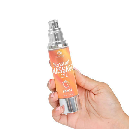 Hand holding a bottle of Sensual Massage Oil Peach 50 ml with orange label and silver pump, designed for intimacy and relaxation.