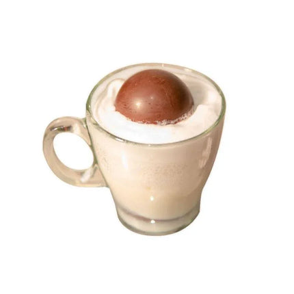 Hot milk with a partially melted Sex Bombs Chocolate releasing marshmallows, in a glass cup.