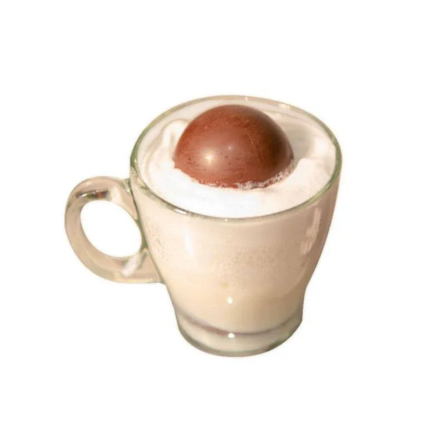 Hot milk with a partially melted Sex Bombs Chocolate releasing marshmallows, in a glass cup.