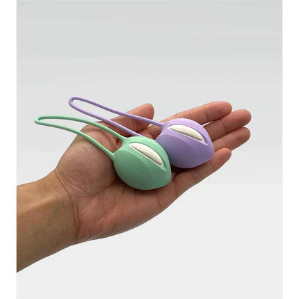 Hand holding two Kegel balls in pastel colors, including Smartball uno Kegel Ball White/Pastel Lilac, for pelvic floor strengthening.