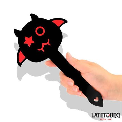 Hand holding a black and red Spanking Paddle 25.2 cm from Latetobed BDSM Line with playful face design.